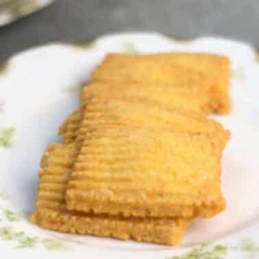 Four rectangular cheese straws arranged on a decorative plate with floral patterns.
