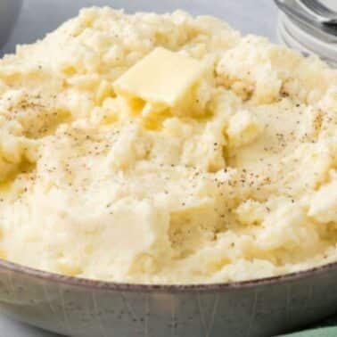 A bowl of mashed potatoes with a pat of butter on top, garnished with pepper.