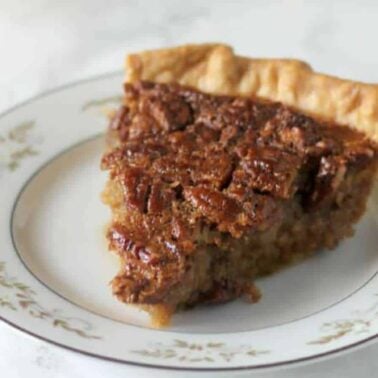 A slice of pecan pie, an old-fashioned dessert that never goes out of style, graces a decorative plate on a marble surface.
