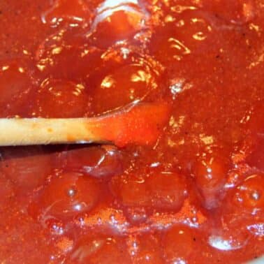 A wooden spoon stirring a pot of barbecue sauce with visible bubbles.