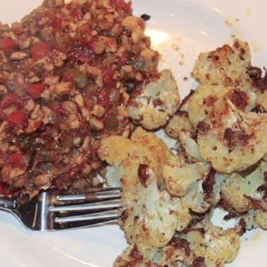 A plate with a serving of mixed vegetable and bean dish on the left and roasted cauliflower on the right, with a fork beside the food.