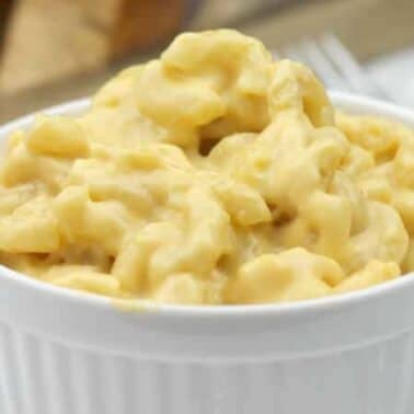 A white ramekin filled with creamy macaroni and cheese on a light background.