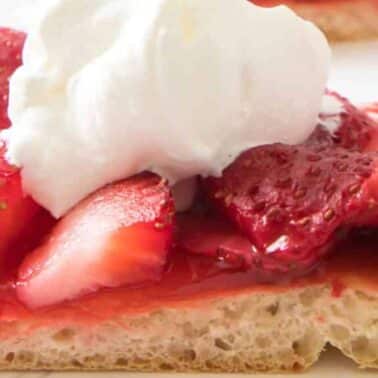 Close-up of a strawberry pizza slice topped with sliced strawberries and a dollop of whipped cream on a light-colored crust.