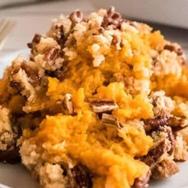 A serving of sweet potato casserole with a crumbly pecan topping on a white plate.