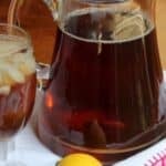 A glass and pitcher of iced tea sit on a cloth, with a lemon nearby.