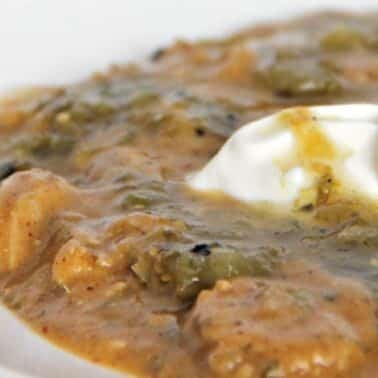Close-up of a bowl of white chicken chili with chunks of meat and dollops of sour cream on top.