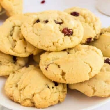 A plate of several crumbly white chocolate cookies with visible cranberries , placed on a white surface.