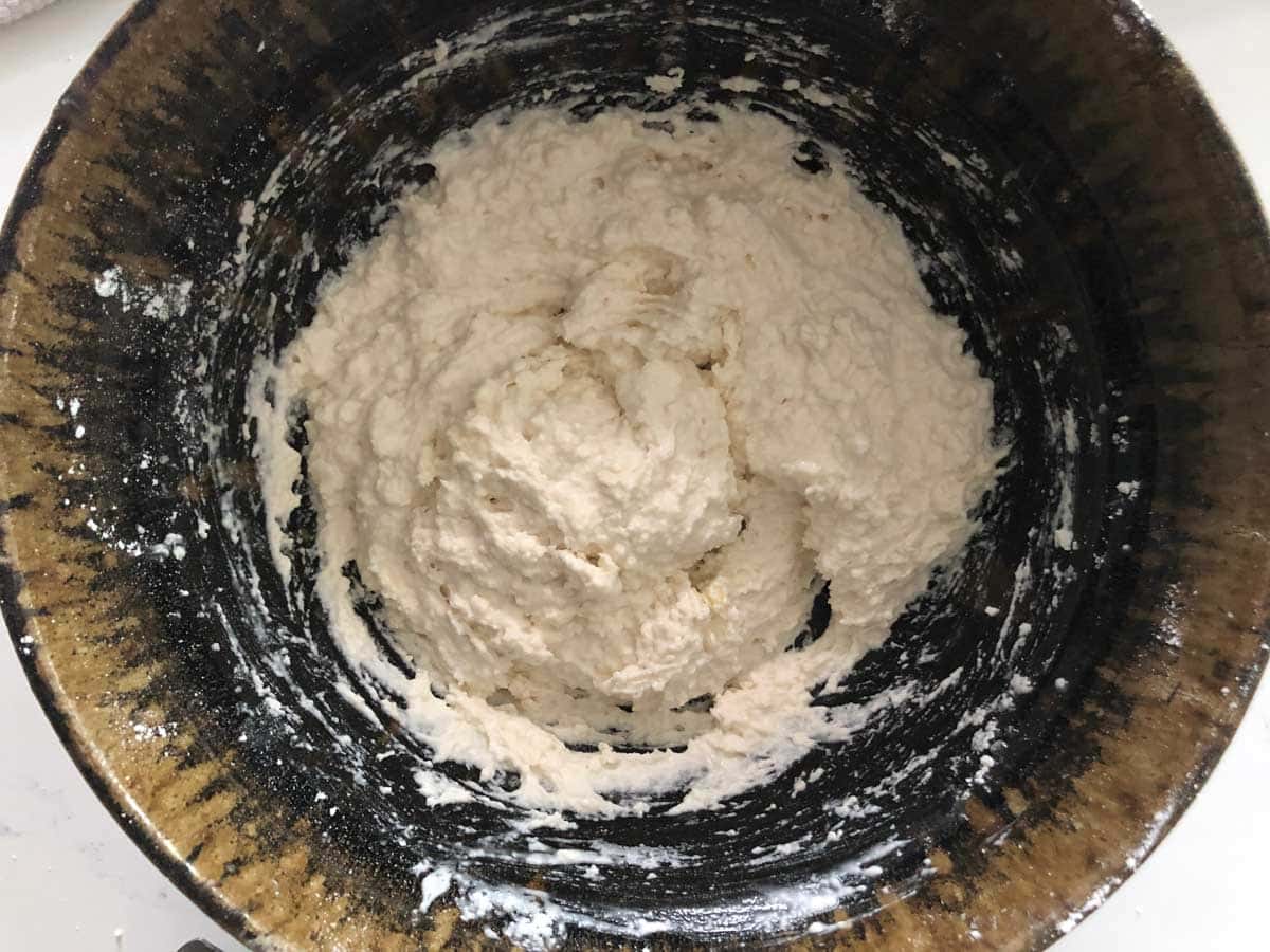 A round ceramic bowl contains a thick, white, roughly mixed dough or batter.