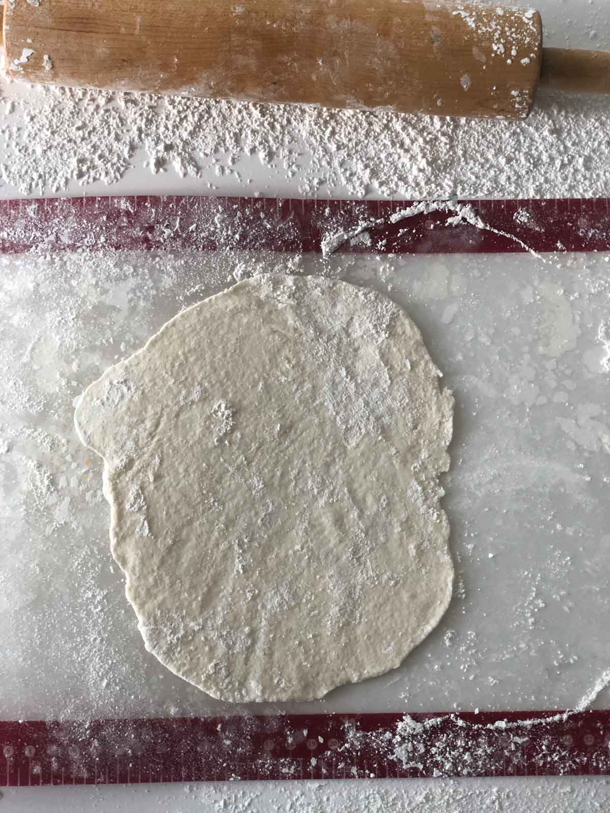 A flat dough covered in flour is placed on a floured surface with a rolling pin nearby.