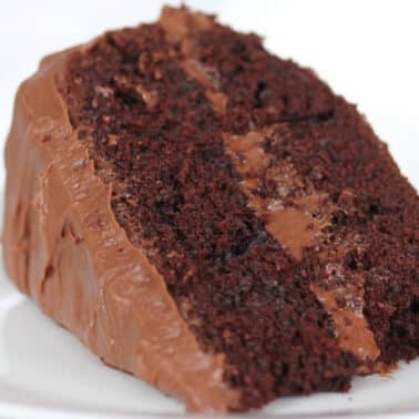 A slice of rich chocolate cake with chocolate frosting on a white plate.