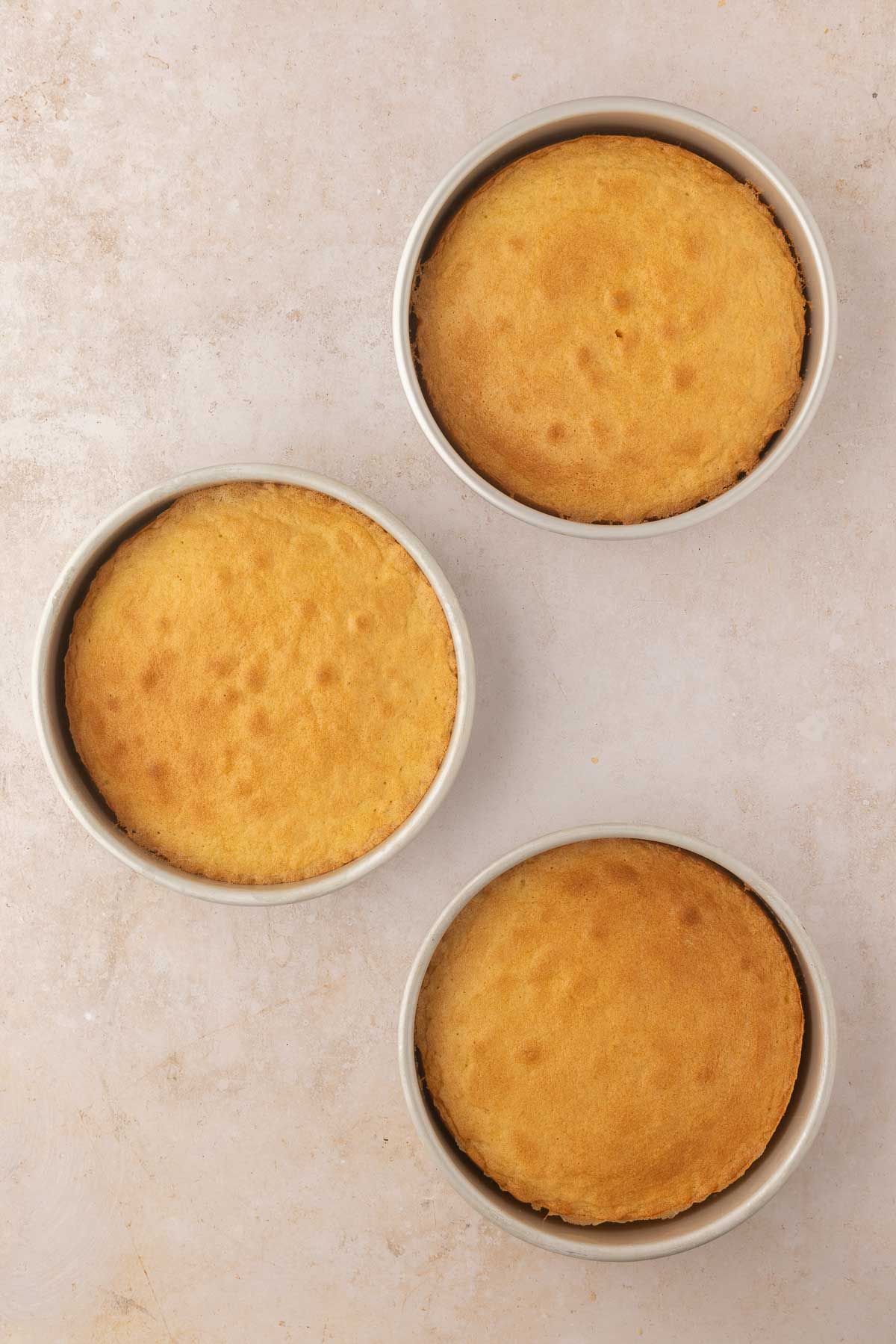 Three round, golden-brown cakes in pans on a light countertop.