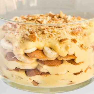 Layered homemade banana pudding with vanilla wafers and creamy custard in a clear glass bowl, topped with crushed nuts.