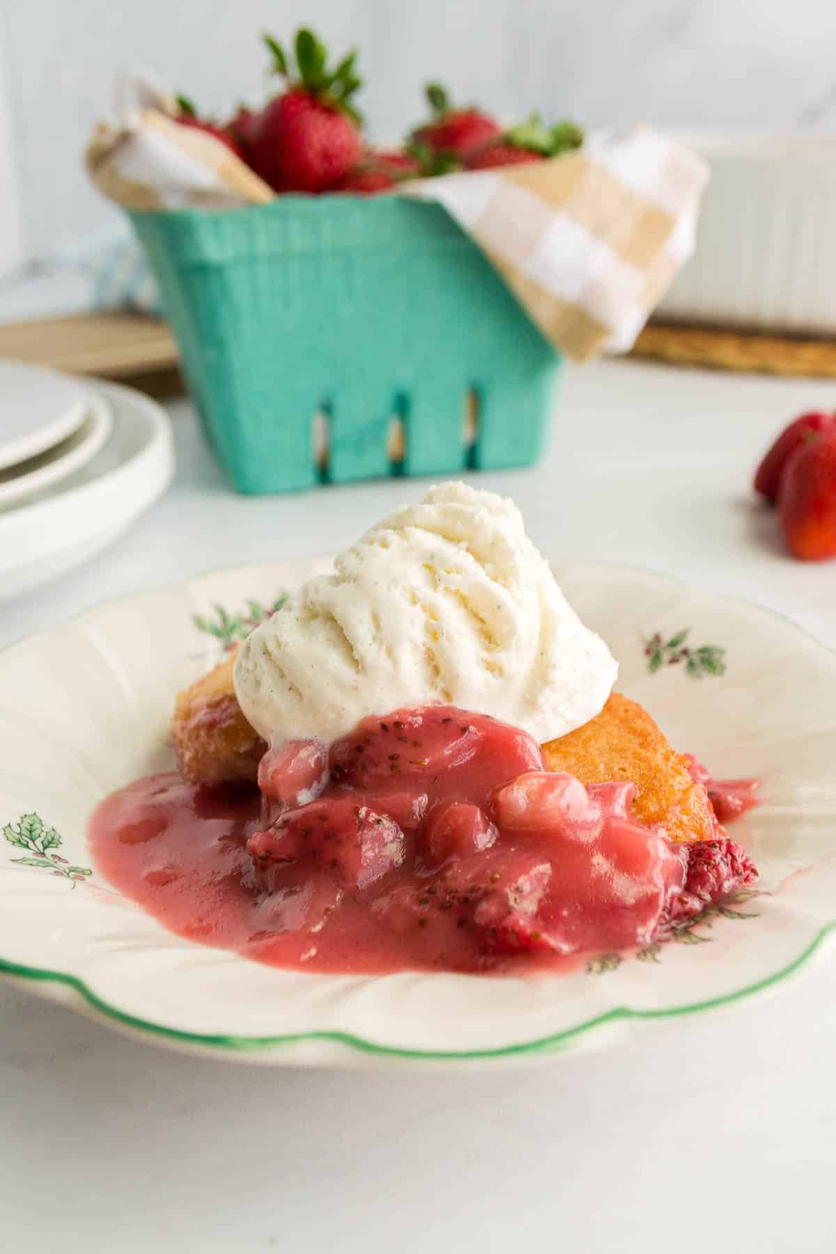 A plate with a dessert featuring a scoop of vanilla ice cream on top of a pastry with red fruit sauce, accompanied by a basket of strawberries in the background.