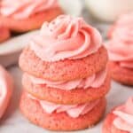 Three pink cookies stacked on top of each other, each with a swirl of pink frosting, placed on a white surface.