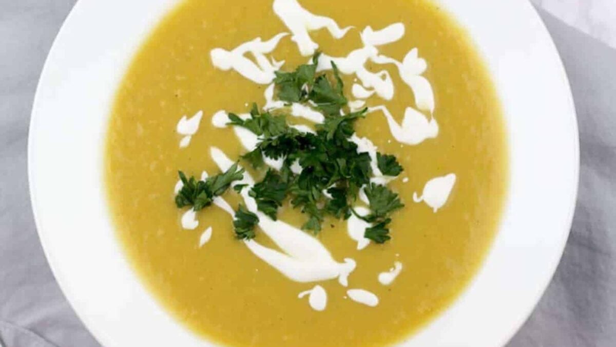 A bowl of yellow soup made from flavorful squash, garnished with a drizzle of cream and fresh chopped parsley—a delightful addition to simple squash recipes.