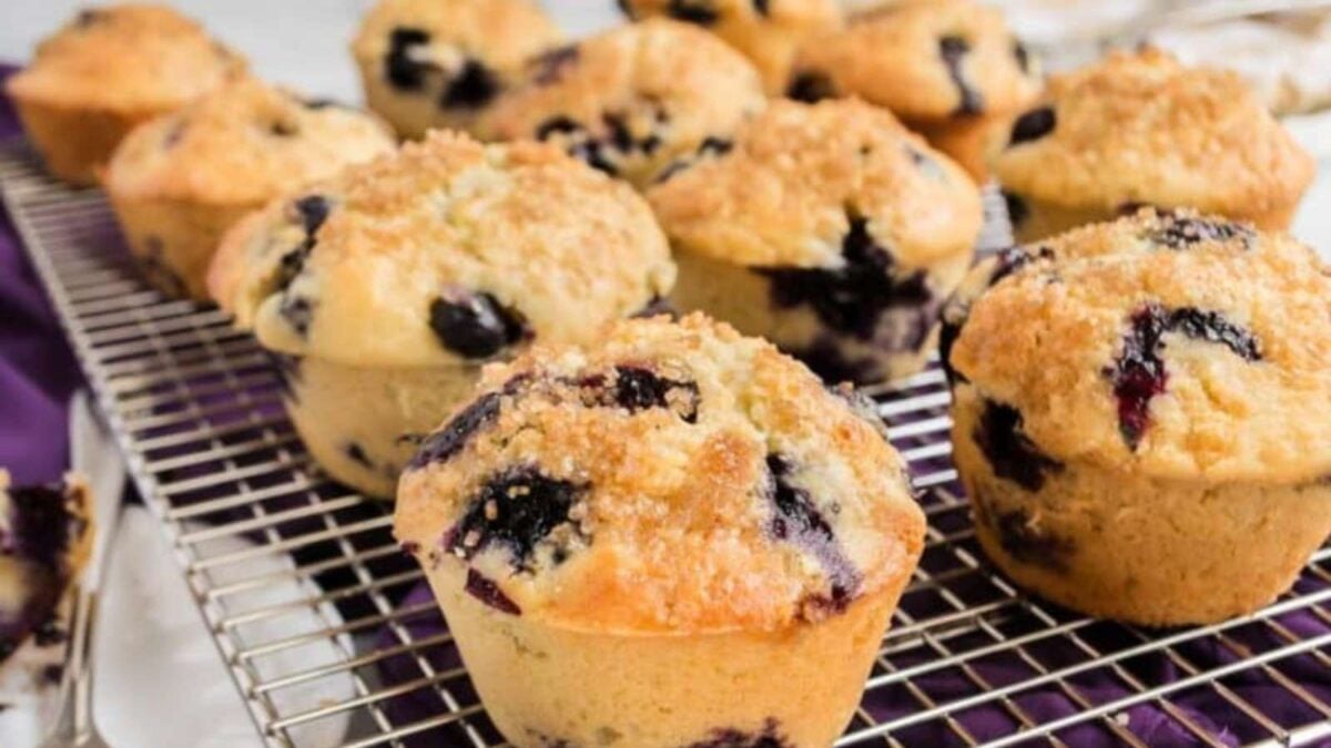 A batch of blueberry dessert muffins with crumb topping is cooling on a metal wire rack, perfect for fans of sweet muffin recipes.