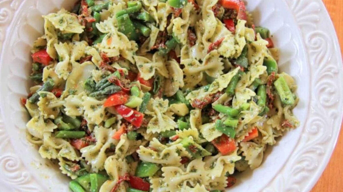A bowl of farfalle pasta mixed with chopped red bell peppers, green beans, sun-dried tomatoes, and herbs makes a vibrant and creative pasta salad.