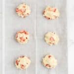 Six unbaked strawberry scones are arranged on a baking sheet lined with parchment paper, ready to go into the oven.