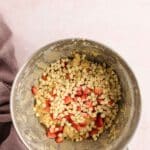 A mixing bowl containing cookie dough with white chocolate chips and chopped strawberries on a light pink surface.