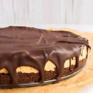 A close-up of a chocolate-covered peanut butter cheesecake with a cookie crust, resting on parchment paper.