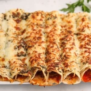 A close-up of baked enchiladas topped with melted, browned cheese and herbs on a white plate.