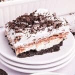 A layered dessert bar with an Oreo cookie crust, creamy layers, whipped topping, chocolate pudding, and chocolate chips on a white plate.