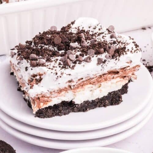 A layered dessert bar with an Oreo cookie crust, creamy layers, whipped topping, chocolate pudding, and chocolate chips on a white plate.