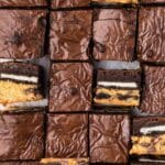 Rows of chocolate brownies, some cut open to reveal layers of cookie dough, Oreo cookies, and chocolate brownie.