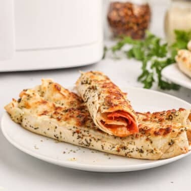 Two baked pizza roll-ups with herbs on a white plate, next to a bowl of marinara sauce.