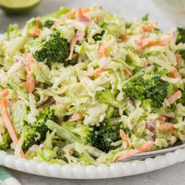 A plate of broccoli slaw with shredded broccoli, carrots, and red onions, mixed with a creamy dressing, served with a fork.