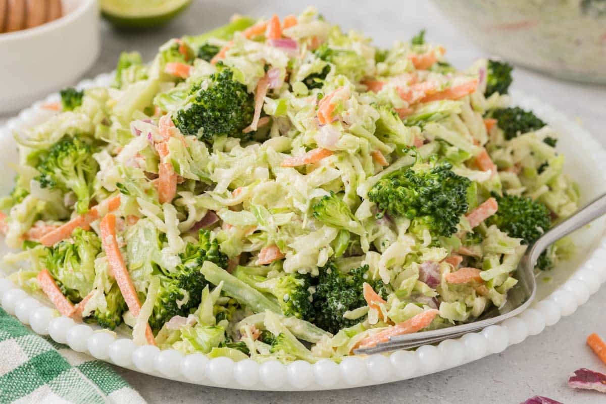 A plate of broccoli slaw with shredded broccoli, carrots, and red onions, mixed with a creamy dressing, served with a fork.