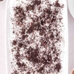 A rectangular dish filled with a dessert topped with whipped cream, chocolate chips, and crushed chocolate cookies.