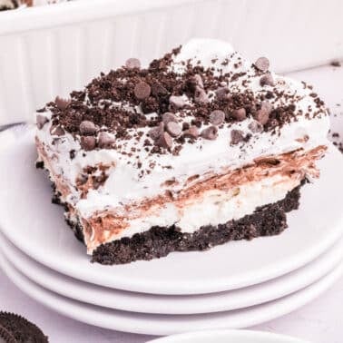 A slice of layered dessert with a chocolate cookie crust, creamy filling, chocolate pudding, whipped topping, and chocolate chips on a white plate.