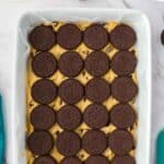 A baking dish lined with chocolate chip cookie dough topped with a layer of whole chocolate sandwich cookies, ready to be baked.