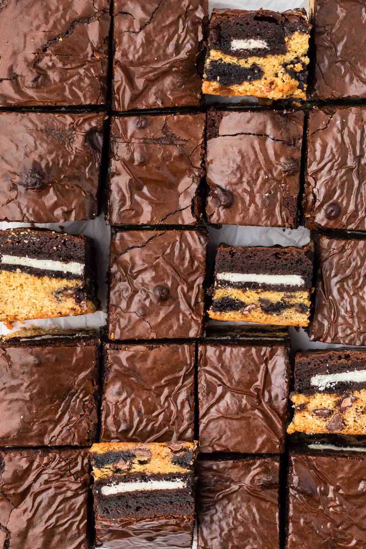 Rows of chocolate brownies, some cut open to reveal layers of Oreo cookies and cookie dough inside.