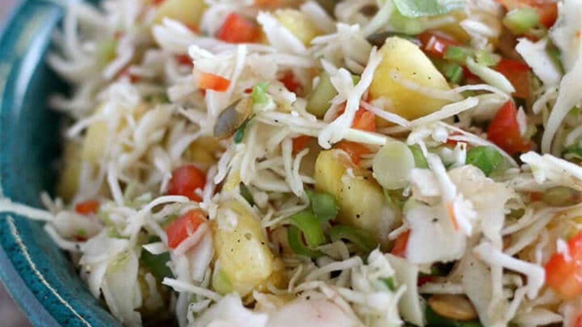 Close-up of a bowl filled with coleslaw featuring shredded cabbage, diced red and green peppers, pineapple chunks, and black pepper—an ideal side dish for any summer cookout.
