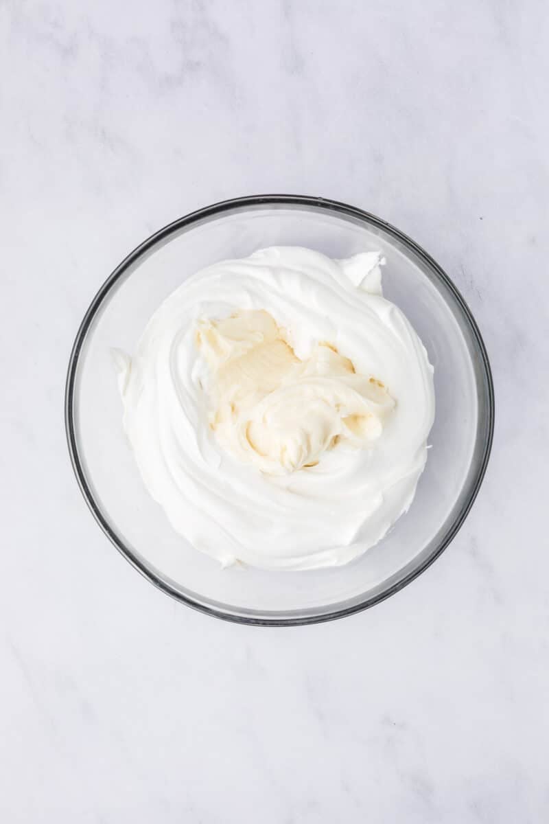 A glass bowl filled with whipped cream cheese and whipped topping on a white marble surface.
