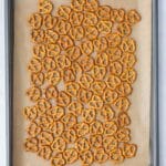 A baking sheet lined with parchment paper holds a scattered layer of small pretzel twists.
