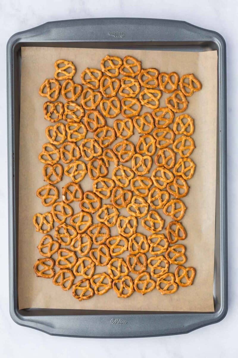 A baking sheet lined with parchment paper holds a scattered layer of small pretzel twists.
