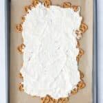 A baking sheet lined with parchment paper holds a layer of pretzels covered with a thick coating of white chocolate.