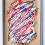 A sheet pan with a base of pretzels covered in white coating and drizzled with red and blue icing, on a piece of parchment paper.