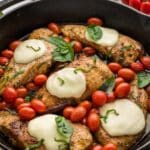Caprese chicken skillet topped with melted mozzarella cheese, garnished with basil leaves and surrounded by cherry tomatoes in a cast iron skillet.