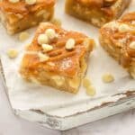 A close-up of caramel blondie squares topped with white chocolate chips and a drizzle of caramel, placed on parchment paper.