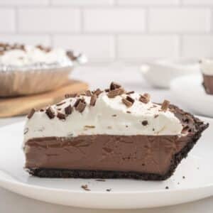 A slice of chocolate cream pie with whipped topping and chocolate shavings, served on a white plate.