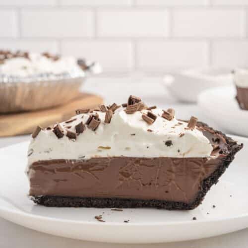 A slice of chocolate cream pie with whipped topping and chocolate shavings, served on a white plate.