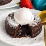 A chocolate lava cake with a molten center is topped with a scoop of vanilla ice cream and dusted with powdered sugar, served on a white plate.