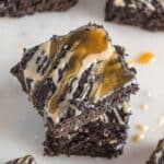 Two espresso brownies stacked, topped with drizzles of caramel and a light tan sauce, on a white surface.