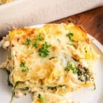 A slice of creamy spinach and cheese lasagna is served on a white plate, garnished with fresh parsley.
