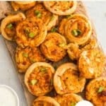 A wooden board topped with baked buffalo chicken pinwheels garnished with green onions, with a bowl of dipping sauce on the side. Text on image promotes the recipe as quick and easy.