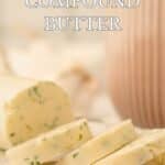 Sliced garlic and herb compound butter on parchment paper, with a blurred pink-striped container and green herbs in the background.